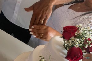 Foto mostra um homem e uma mulher mostrando suas mãos com aliança de casamento.