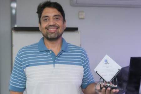 Foto mostra um homem sorrido e segurando o prêmio recebido do Google.