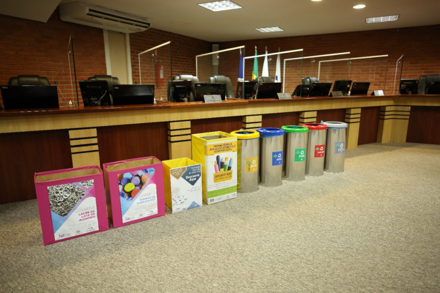Foto mostra diversos recipientes para coletiva seletiva exibidos em frente à bancada do Plenário do TJTO.