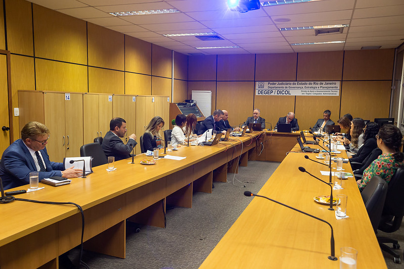 Foto mostra momento da reunião, com participantes sentados em mesa em U em sala do TJRJ.