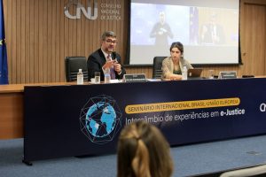 Foto da mesa de encerramento do evento no auditório do CNJ, com o secretário-geral do CNJ, Valter Shuenquener, falando e, a seu lado, a chefe da Seção Politica, Econômica e de Informação da Delegação da União Europeia para o Brasil, Domenica Bumma.