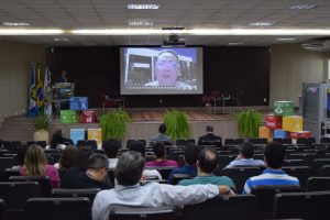 Foto mostra momento da abertura da audiência pública no auditório do TJMT, no qual a presidente Maria Helena Póvoas está falando em um telão projetado no palco.