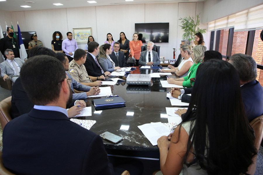 Foto mostra momento do encontro para assinatura da cooperação, com as pessoas sentadas em volta de um comprida em uma sala do TJTO.