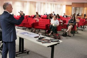 Foto de momento do curso em auditório da Enfam, sendo possível ver o instrutor falando e parte do público sentado.