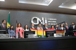 Foto no Plenário do CNJ durante o evento mostra a cantora Daniela Mercury ao centro, ladeada pelo ministro Fux, pelo conselheiro Marcio Freitas e outras autoridades do CNJ, todos segurando uma bandeira do movimento LGBTQIA+.
