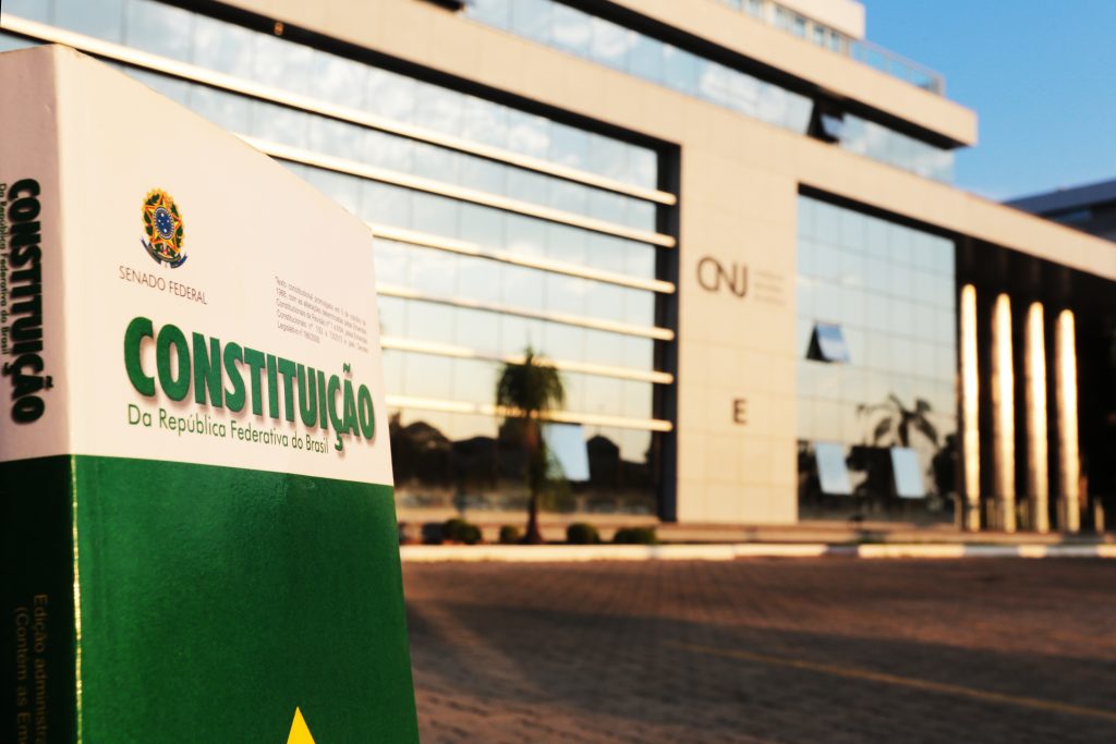 Imagem da Constituição Federal tendo ao fundo a fachada do Conselho Nacional de Justiça (CNJ)