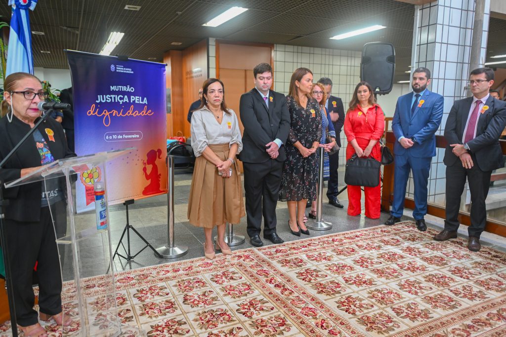 Homens e mulheres reunidos ao redor de um tapete e uma mulher discursando