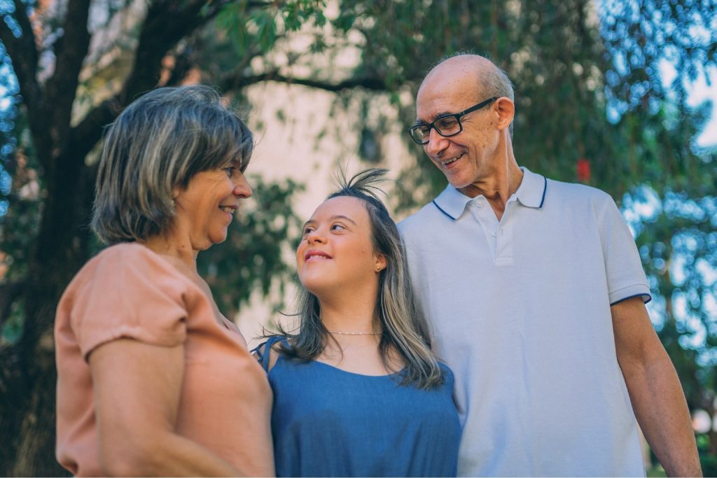 Fotografia de uma família composta por um homem, uma mulher, e uma menina. No fundo há árvores desfocadas 